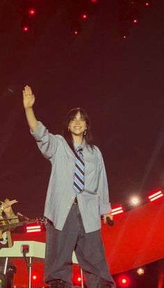 a man standing on top of a stage with his arms in the air and one hand up