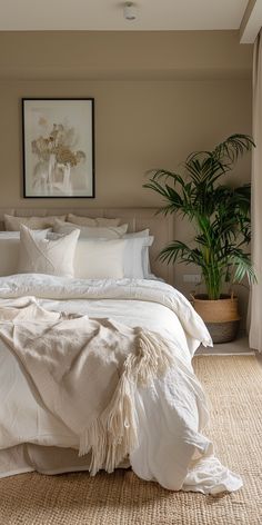 a bed with white linens and pillows in a bedroom next to a potted plant