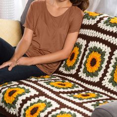 a woman sitting on top of a couch covered in a crochet granny blanket