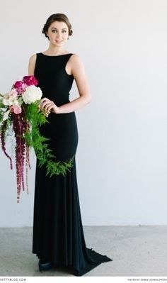 a woman in a long black dress holding a flower bouquet and posing for the camera