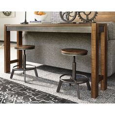 two stools sitting under a table in front of a gray couch with a clock on the wall