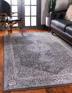 a living room area with black leather couches and rugs on the hardwood floor