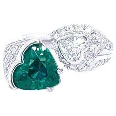 Behold the elegance of this exquisite platinum fashion ring, adorned with a magnificent 3 carat Heart green vivid emerald and a dazzling 0.50 carat Heart Shape Diamond. The green emerald, delicately heated, takes center stage, cradled in a semi-bezel and prong setting that accentuates its natural beauty. Complementing the sapphire, the heart shape diamond sits gracefully in a bezel setting, embraced by a halo of round brilliant diamonds that shimmer with brilliance. Additional diamonds grace both sides of the shank, totaling 0.60 carats in weight, boasting vs1/vs2 clarity and F color. This enchanting ring embodies sophistication and refinement, capturing the essence of timeless glamour and luxury. Heart Shape Diamond Ring, Heart Shaped Diamond Ring, Emerald Ring Engagement Diamond, Emerald Diamond Ring, Modern Engagement Rings, Jewels Rings, Family Jewellery, Heart Shaped Rings, Heart Shaped Diamond