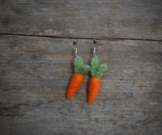 two tiny carrots with green leaves hanging from hooks on a wooden surface, one is made out of felt and the other has silver ear wires