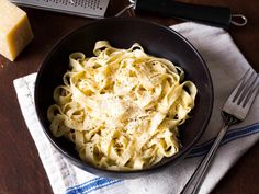 a black bowl filled with pasta on top of a table next to cheese and fork