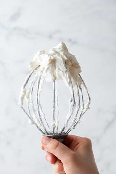 a hand holding a wire whisk filled with whipped cream on top of a white counter