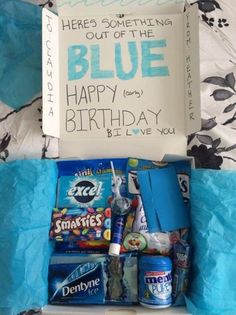 a birthday gift box filled with candy and blue tissue paper on top of a bed