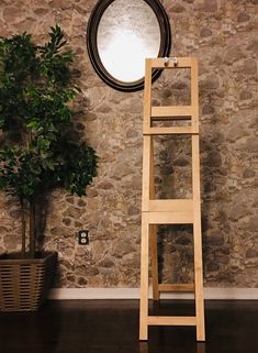 a ladder leaning against a stone wall next to a potted plant and round mirror