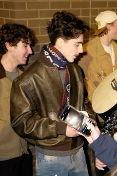 two men are talking to each other while one man is holding a cell phone and wearing a leather jacket