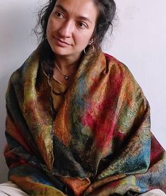 a woman sitting on top of a bed covered in a multicolored shawl