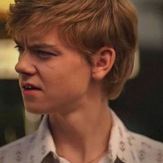 a young man with blonde hair wearing a white shirt and looking off into the distance