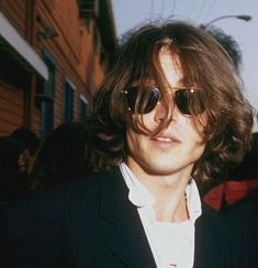 a man with long hair and sunglasses standing in front of a building