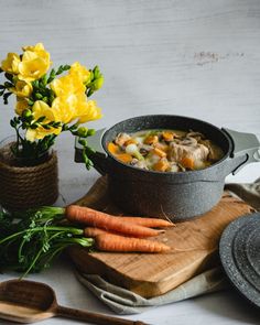 a bowl of soup with carrots and flowers on a cutting board next to it