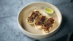 three pieces of food on a plate with a lime wedge next to it and another piece of lime in the background