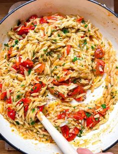 pasta with tomatoes and parsley in a skillet being stirred by a spatula