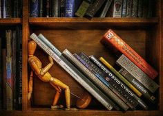 a wooden figurine sitting on top of a book shelf filled with lots of books