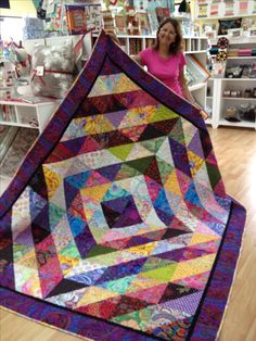 a woman holding up a colorful quilt in a store