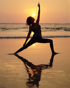 a woman doing yoga on the beach at sunset