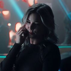 a woman talking on a cell phone in a dark room with neon lights behind her