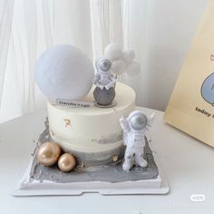 a white cake with an astronaut on top and balloons in the air next to it