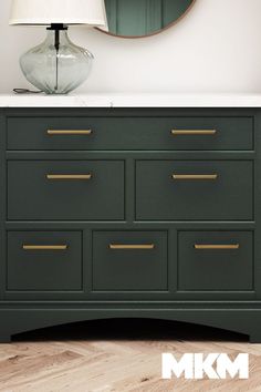 a green dresser with gold handles and a round mirror on the wall next to it