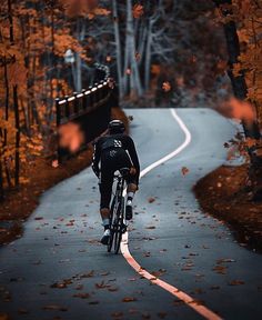 a bicyclist riding down a road in the fall with leaves on the ground