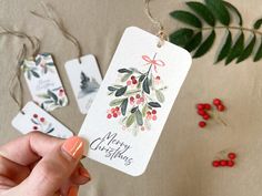 a hand holding a merry christmas tag with holly and berries on it next to some red berries