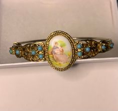 "I love this bracelet. There is nothing like it to be found today.  This sweet vintage gold tone bangle bracelet has a porcelain Victorian scene on it.  The scene is enhanced with gold scroll and 10 beautiful turquoise cabochons to the sides. I could not tell you if the turquoise is faux or real but they look great. Porcelain face shows a woman and a man embracing. Side Closure still good on bangle and it is ready to wear. It is for a 7\" wrist or smaller. Very pretty for both young girl or adult. No makers mark. Ready to wear. Comes with box and would make a lovely gift." Vintage Turquoise Bracelets As Gift, Vintage Oval Cuff Bracelet As Gift, Antique Oval Bangle Gift, Vintage Turquoise Bangle As A Gift, Victorian Style Bracelet With Vintage Charm For Gift, Antique Enamel Bracelets As Gift, Victorian Style Metal Bangle Bracelet, Vintage Turquoise Enamel Jewelry, Vintage Enamel Cuff Bracelet As Gift