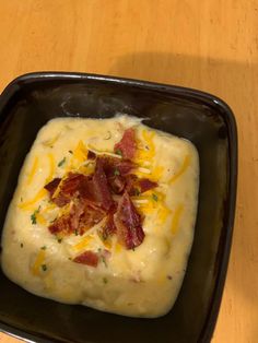 a black bowl filled with mashed potatoes topped with bacon and cheddar cheese