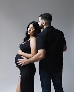 a man and woman standing next to each other with their arms around the pregnant belly