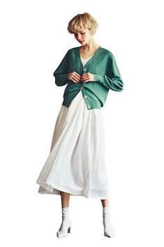 a woman wearing a green cardigan and white skirt