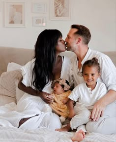 a man and woman kissing their children on the bed