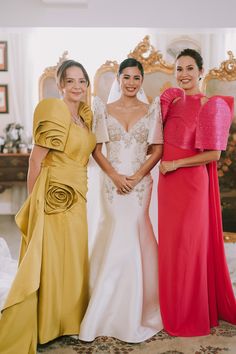 three women standing next to each other in formal dresses and one is holding her arm around the other