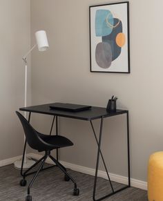 a black desk and chair in a room with a painting on the wall behind it