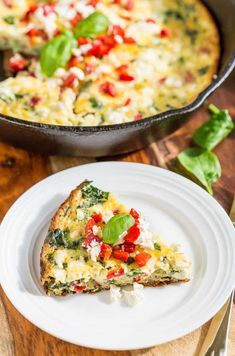 a slice of quiche on a plate next to a skillet with spinach and tomatoes