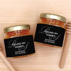 two jars of honey sitting on top of a wooden table next to a brush and spoon