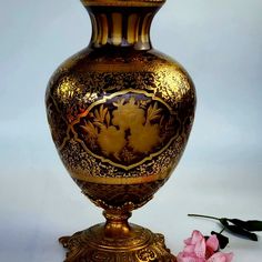 a gold vase sitting on top of a table next to some pink flowers and leaves