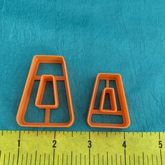 two orange plastic shapes sitting on top of a blue surface next to a measuring ruler