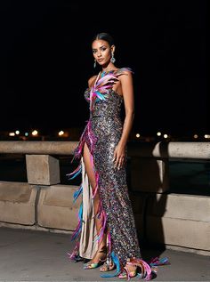 a woman in a long dress standing next to a stone wall at night with her hands on her hips