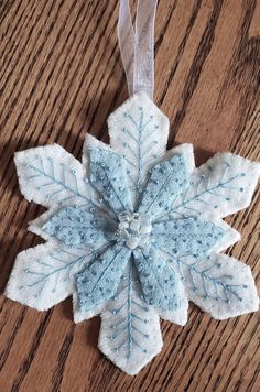 a blue and white snowflake ornament hanging on a wooden table with ribbon