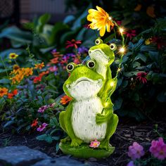 two green frogs sitting on top of each other in front of some flowers and plants