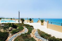 an outdoor swimming pool next to the ocean with plants and rocks in the foreground