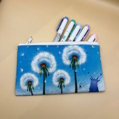 a pencil case with three dandelions on it and four pens in the holder