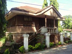 an old wooden house sitting on the side of a road in front of trees and bushes