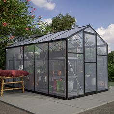 a small greenhouse sitting on top of a cement floor next to a bench and potted plants