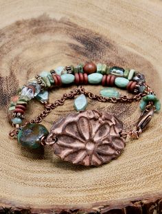 This multi-stranded bracelet has a Southwestern Boho vibe to it.  The focal feature is the scalloped oval shaped ceramic piece with a flower design.  This ceramic piece is handmade, although not done so by me.  The second largest bead is a turquoise stone on hand-crafted copper wire.  The strands are comprised of natural stone and glass beads in turquoise, red brick, and brown, and a small linked antiqued copper chain embellished with dangling leaf beads.   A dangling antiqued copper bird charm Ceramic Leaf, Bracelets Ideas, Bead Flower, Southwestern Boho, Bird Beads, Jewerly Beads, Beautiful Bracelets, Bead Necklaces, Silver Jewelry Design