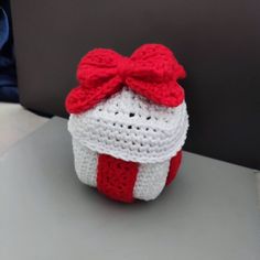 a crocheted basket with a red bow on it sitting on a table next to a laptop