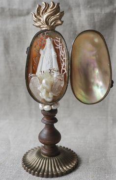 an old fashioned vanity mirror with shells and pearls on it's stand, in front of a gray background