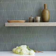 flowers and vases sit on a shelf in the corner of a room with blue tiles