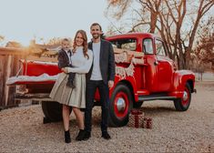 a man, woman and child standing in front of an old red truck